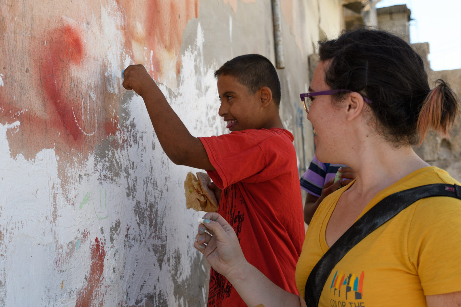 Betty draws on a wall with a child in Jerash refugee camp.