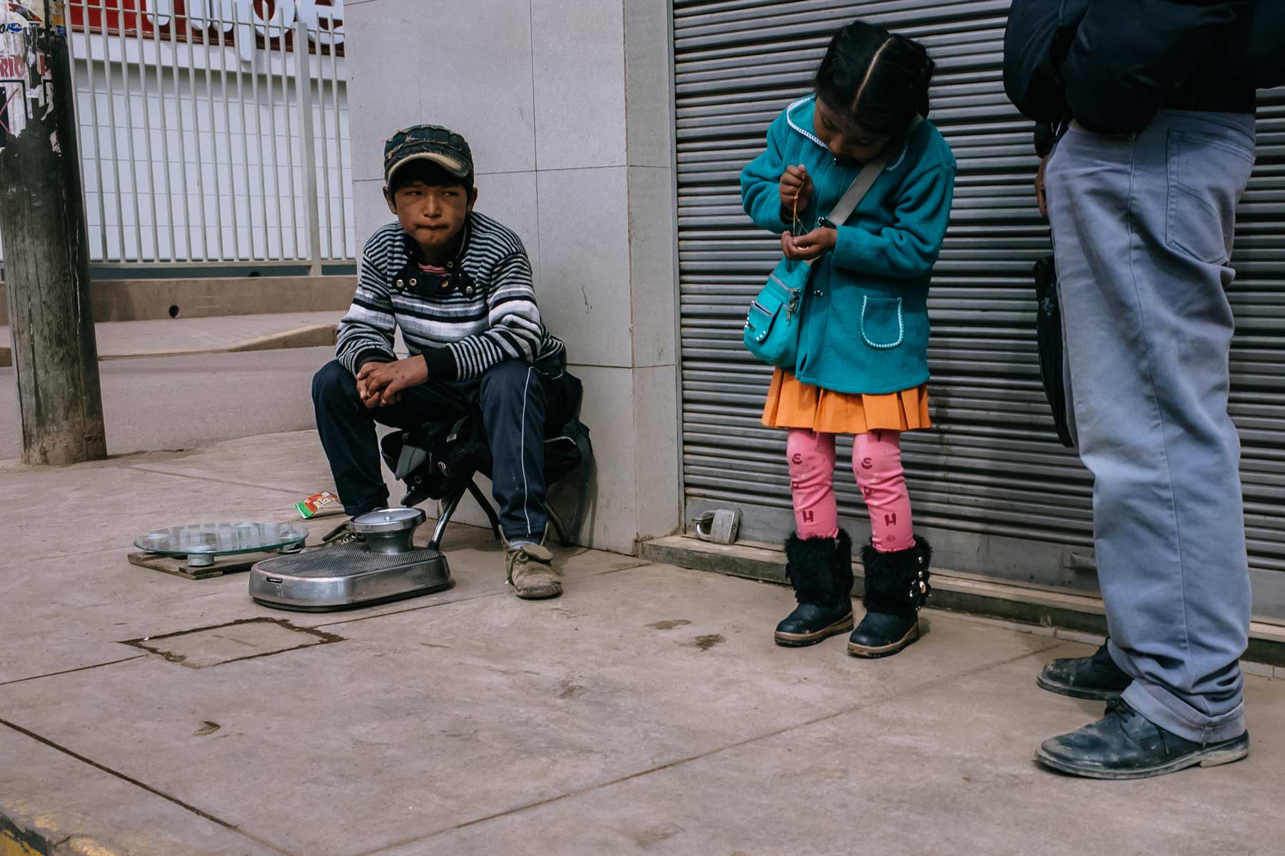 A working boy stares at a girl waiting to cross the street playing with a gold necklace in Juliaca.