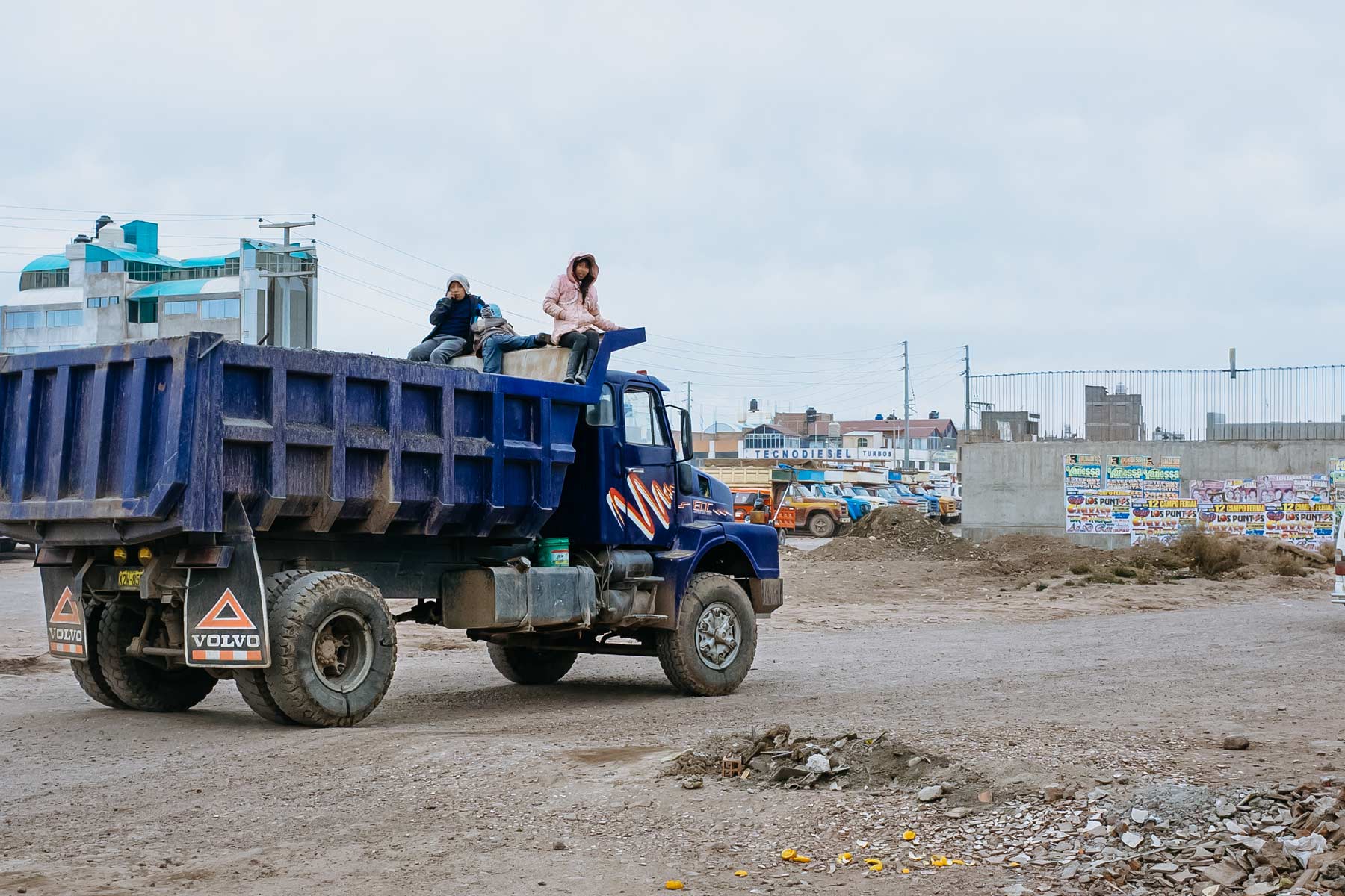 Three children riding on the back of a mining dump truck in Juliaca.